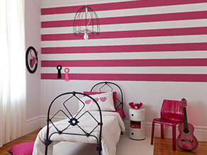 little_kids_pink_striped_feature_wall_bedroom_black_bed_frame_pink_chair_white_rug_timber_floor